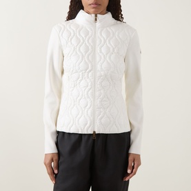 Model wearing Moncler natural cardigan with quilted front panel, zip fastening, and ribbed knit sleeves, styled with black trousers