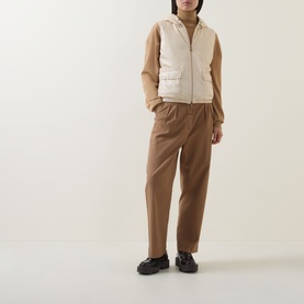 Model wearing Moncler beige padded gilet with hood and utility pockets, styled with tan trousers and black chunky loafers