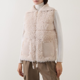 Model wearing Moncler beige shearling gilet with ribbed knit pocket detail and drawstring hem, styled with white roll-neck and khaki trousers