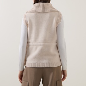 Model wearing Moncler beige gilet, back view, with ribbed turtleneck collar and side pockets, styled with white long-sleeve top and taupe trousers