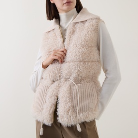 Model wearing Moncler beige shearling gilet with knit lower panel and drawstring hem, styled with white ribbed turtleneck
