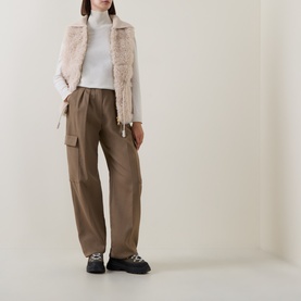 Model wearing Moncler beige faux fur gilet, styled with white turtleneck, taupe cargo trousers and black chunky loafers.