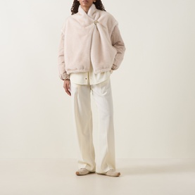 Model wearing Moncler beige faux fur padded jacket with white wide-leg trousers and cream slip-on shoes.