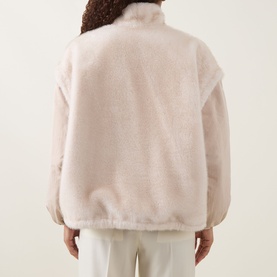 Model wearing Moncler beige faux fur jacket, back view, styled with white trousers
