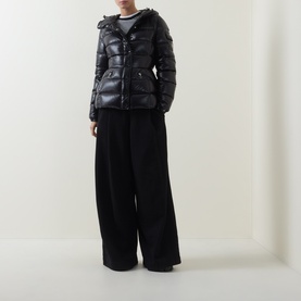 Model wearing Moncler black glossy puffer jacket with detachable hood, styled with wide-leg black trousers and striped top