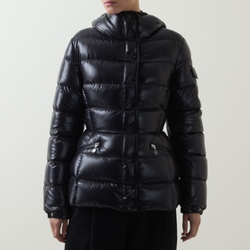 Model wearing Moncler black glossy quilted down jacket with hood, cinched waist, and zip pockets
