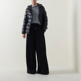 Model wearing Moncler black quilted down jacket with glossy finish, styled with wide-leg black trousers and grey top.