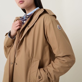 Model wearing Moncler brown hooded jacket with logo arm badge, styled with a light blue striped shirt and scarf.