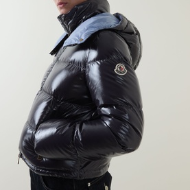 Model wearing Moncler Niveole Glossy Down Jacket in navy, boudin quilted with detachable hood and logo patch, light blue hood lining visible.