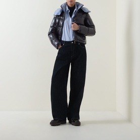 Model wearing Moncler Niveole Glossy Down Jacket in navy with detachable hood, styled with blue shirt and black wide-leg jeans.