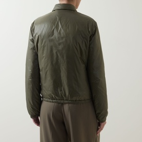 Model wearing Moncler olive padded jacket, rear view, with taupe wide-leg trousers. Zip-front, ribbed hem, lightweight quilted shell.