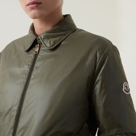 Model wearing Moncler olive padded jacket, close-up showing gold zip, shirt collar, and logo badge on sleeve.