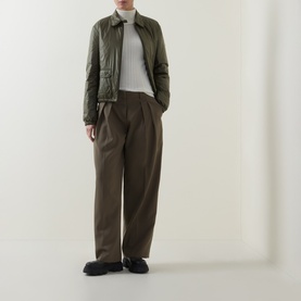 Model wearing Moncler olive polyamide jacket with white ribbed top and wide-leg brown trousers, styled with black loafers.
