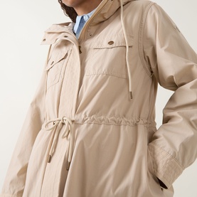 Model wearing Moncler beige jacket with hood, drawstring waist, chest pockets, and snap button detail, styled with blue shirt