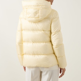 Model wearing Moncler light yellow quilted down jacket, rear view showing hood and puffer panels, styled with white trousers