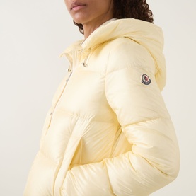 Model wearing Moncler light yellow quilted down jacket with hood, branded arm badge visible, shiny polyamide finish