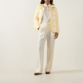 Model wearing Moncler light yellow quilted down jacket with hood, styled with white shirt and wide-leg trousers