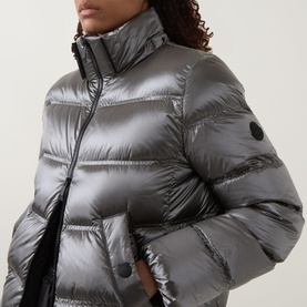 Model wearing Moncler dark grey quilted puffer jacket with high collar, glossy finish, and logo badge on sleeve.