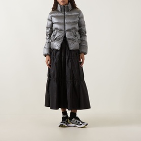 Model wearing Moncler dark grey quilted puffer jacket, styled with black tiered midi skirt and chunky trainers