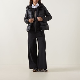 Model wearing Moncler black quilted down jacket with hood, styled with wide-leg black trousers and white shirt.