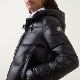 Model wearing Moncler black quilted down jacket with hood, high-neck zip closure and signature logo badge, styled with white shirt