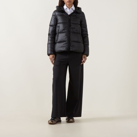 Model wearing Moncler black quilted down jacket with hood, styled with wide-leg black trousers and white shirt.