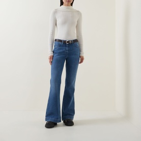 Model wearing Moncler medium blue flared jeans with white belt, styled with a white ribbed turtleneck top and black shoes.