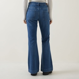 Model wearing Moncler medium blue high-rise flared jeans, rear view, styled with a grey top and black shoes.