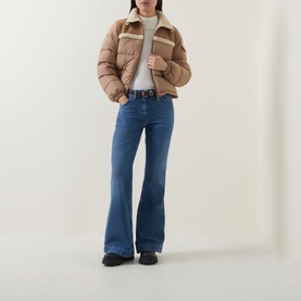 Model wearing Moncler medium blue flared cotton jeans, styled with a camel puffer jacket and black loafers