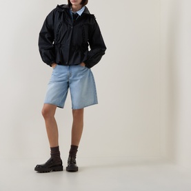 Model wearing Moncler black polyamide parka with hood, styled with light blue denim shorts and chunky dark brown lace-up boots.