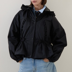 Model wearing Moncler black polyamide parka with ruffle trim, drawstring waist, and hood, styled with blue jeans and light blue shirt.