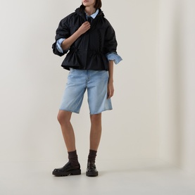 Model wearing Moncler black polyamide parka with ruched neckline, styled with light blue denim shorts and chunky dark brown boots.