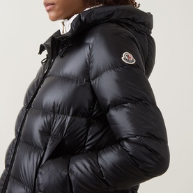 Model wearing Moncler black quilted down parka with hood and branded logo badge, glossy finish