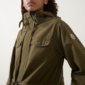 Model wearing Moncler olive parka with hood, chest pockets, drawstring waist, and logo arm badge, in cotton-polyester blend.