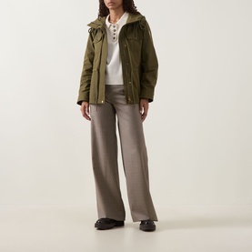 Model wearing Moncler olive parka with hood, styled with white knit top, wide-leg taupe trousers and dark loafers