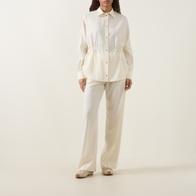 Model wearing Moncler cream shirt with cinched waist detail, styled with matching wide-leg trousers and flat shoes