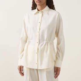 Model wearing Moncler cream shirt with drawstring waist, gold-tone buttons, and pointed collar, styled with cream wide-leg trousers