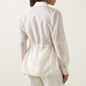 Model wearing Moncler cream shirt, back view, showing drawstring waist detail and button cuffs, styled with matching cream trousers