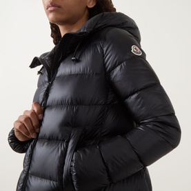 Model wearing Moncler black quilted down parka with hood, zip fastening and logo badge on sleeve, close-up detail view.