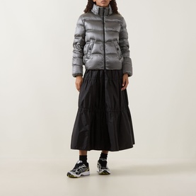 Model wearing Moncler black polyamide midi skirt with tiered hem, styled with a grey puffer jacket and chunky trainers.