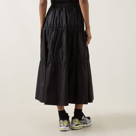 Model wearing Moncler black tiered polyamide midi skirt, styled with grey chunky trainers and black socks.