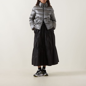 Model wearing Moncler black polyamide tiered midi skirt, styled with a silver puffer jacket and chunky trainers.
