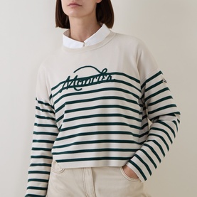 Model wearing Moncler lime stripe sweatshirt with branded script logo, styled with a white collared shirt underneath and cream trousers.