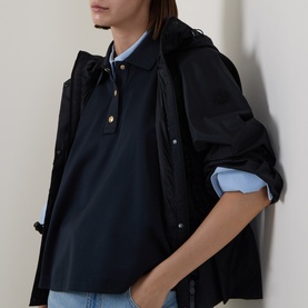 Model wearing Moncler navy cotton polo top, styled with a light blue shirt underneath and black hooded jacket over shoulders.