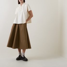 Model wearing Moncler cream cotton polo top with button placket, styled with khaki midi skirt and black loafers.