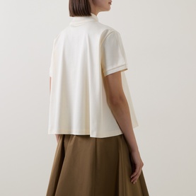 Model wearing Moncler cream cotton top with mock neck and short sleeves, styled with an olive midi skirt. Back view.