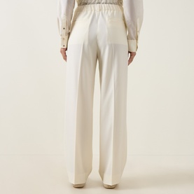 Model wearing Moncler cream wool wide-leg trousers, rear view, styled with a white blouse with gold cufflinks.
