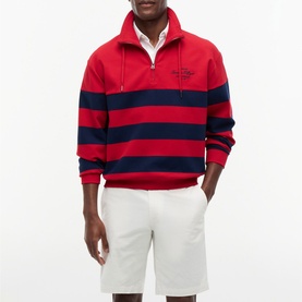 Model wearing Tommy Hilfiger medium red and navy bold stripe half-zip sweatshirt with embroidered chest logo, styled with white shorts.