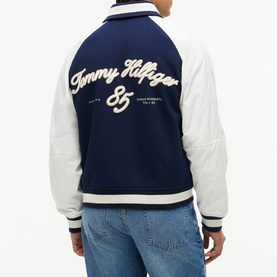 Model wearing Tommy Hilfiger Carbon Navy varsity bomber jacket with white leather sleeves, script logo and ribbed hem, styled with light blue jeans
