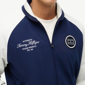 Model wearing Tommy Hilfiger Carbon Navy zip-up track jacket with white contrast sleeves, script logo and circular badge detail.